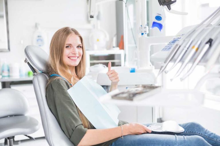 A woman sitting in a dentist chair giving a thumbs up.