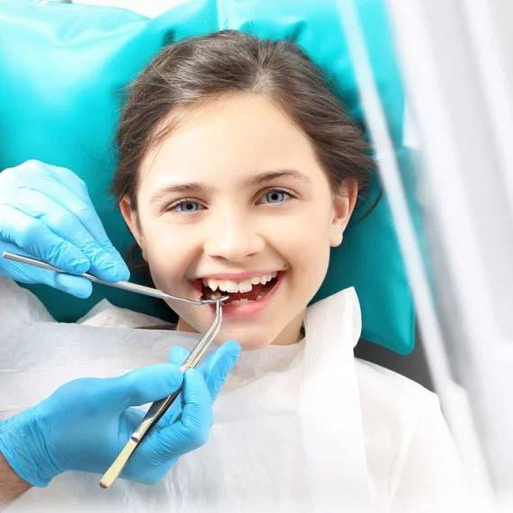 Young girl smiling in dental chair as dentist examines her teeth
